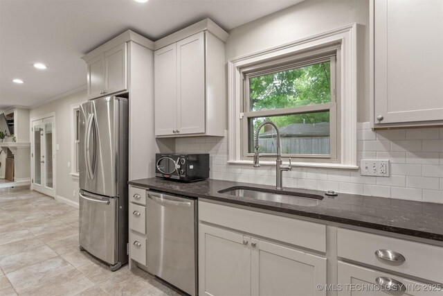 kitchen with appliances with stainless steel finishes, a sink, tasteful backsplash, dark stone counters, and recessed lighting