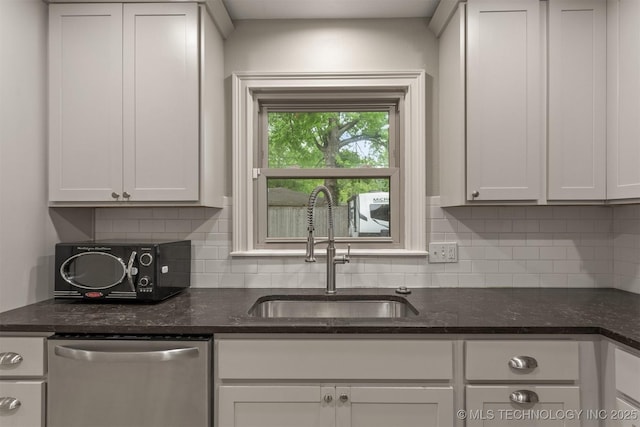 kitchen with dishwasher, a sink, backsplash, and dark stone counters
