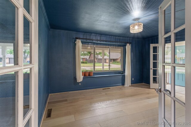 empty room with wood finished floors, baseboards, ornamental molding, and french doors