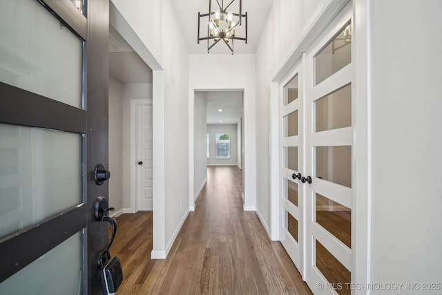 entryway featuring wood finished floors, a chandelier, baseboards, and french doors