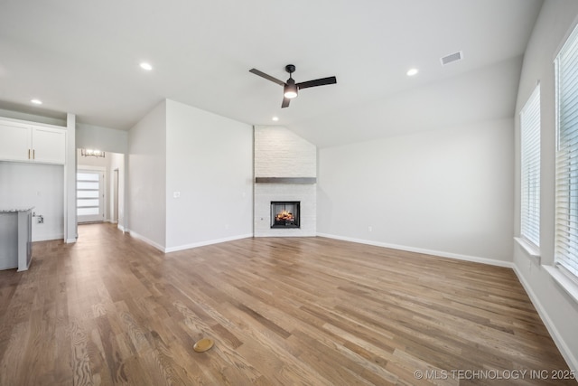 unfurnished living room with a ceiling fan, vaulted ceiling, light wood-style flooring, a large fireplace, and baseboards