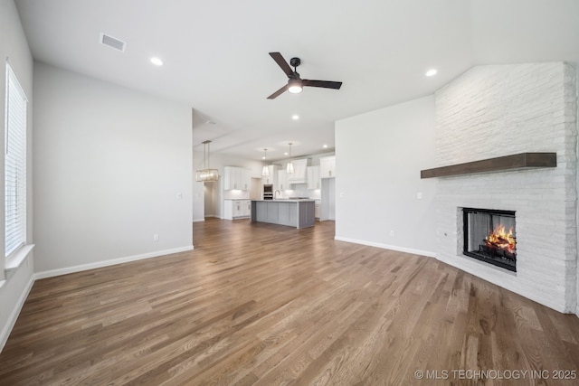 unfurnished living room with ceiling fan, a large fireplace, wood finished floors, baseboards, and recessed lighting