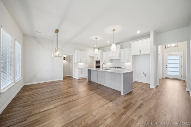 kitchen with a chandelier, baseboards, white cabinets, an island with sink, and recessed lighting