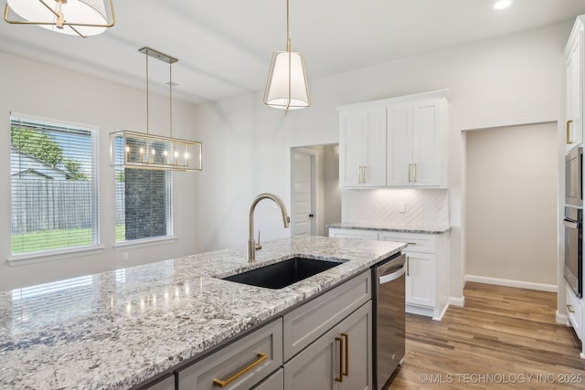 kitchen with a sink, stainless steel appliances, light wood-style flooring, and pendant lighting