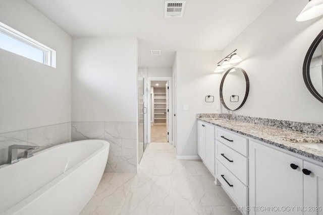 bathroom with marble finish floors, a spacious closet, double vanity, and a freestanding tub