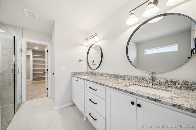 bathroom featuring marble finish floors, a spacious closet, a shower stall, double vanity, and baseboards