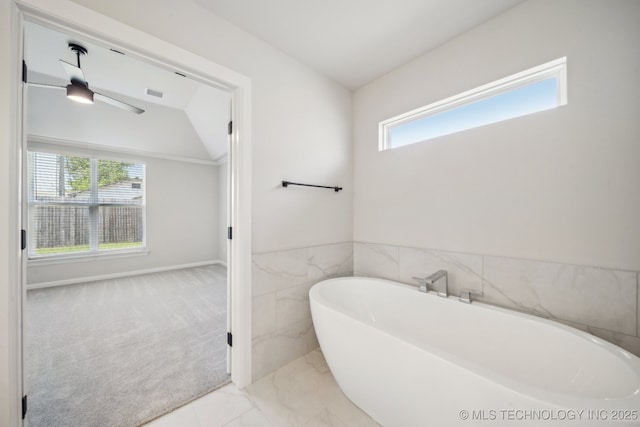 full bathroom with a soaking tub, tile walls, a ceiling fan, and a wainscoted wall