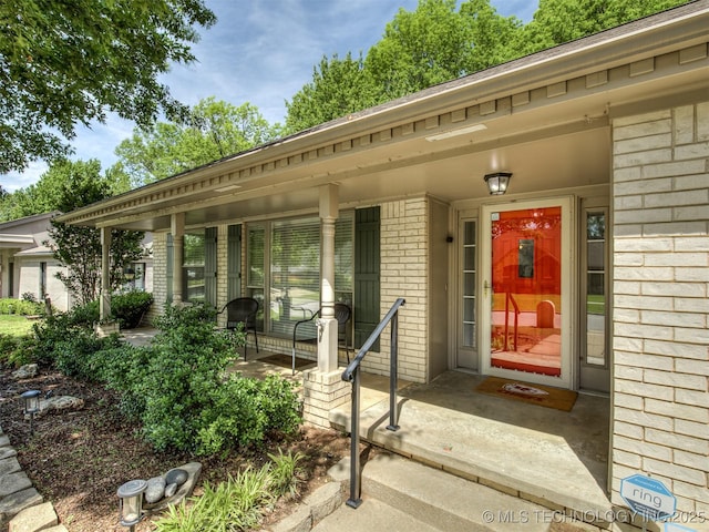 view of exterior entry featuring brick siding and a porch