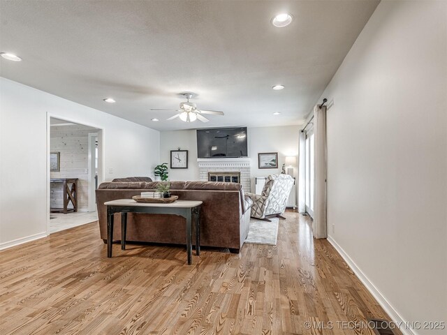 living area featuring light wood-type flooring, a fireplace, a ceiling fan, baseboards, and recessed lighting
