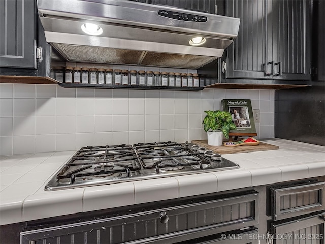 kitchen with extractor fan, tile countertops, backsplash, stainless steel gas cooktop, and dark cabinetry