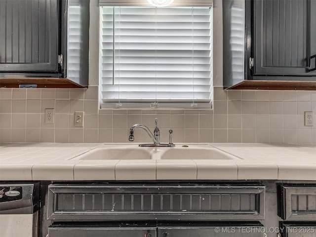 kitchen view of tile counters, a sink, and backsplash