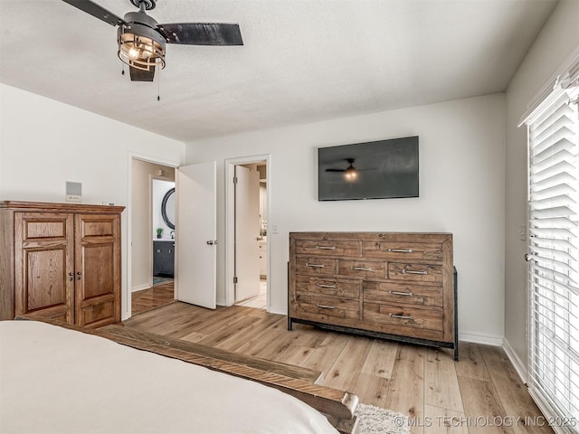 bedroom featuring light wood finished floors, baseboards, a ceiling fan, and ensuite bathroom