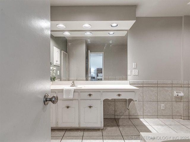 bathroom featuring tile patterned flooring, tile walls, vanity, wainscoting, and recessed lighting