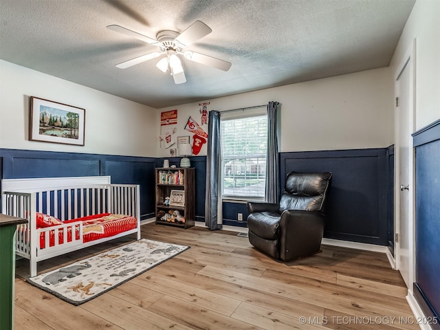 bedroom with a textured ceiling, wainscoting, wood-type flooring, ceiling fan, and a decorative wall
