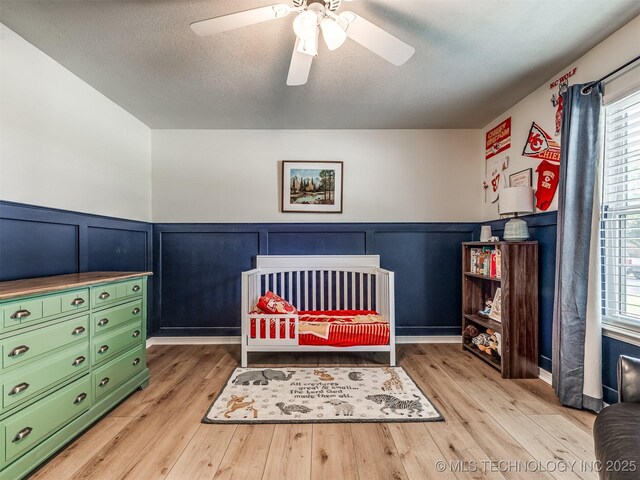 bedroom featuring multiple windows, wood finished floors, a decorative wall, a wainscoted wall, and ceiling fan
