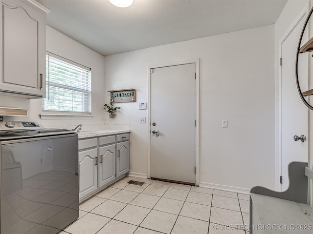 kitchen with gray cabinetry, light countertops, light tile patterned floors, baseboards, and independent washer and dryer