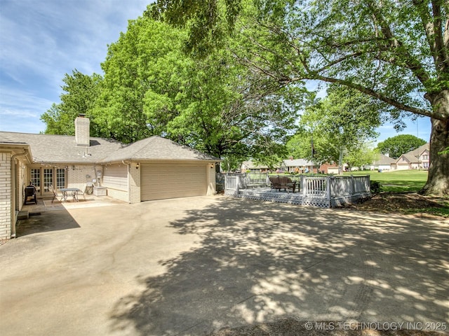 view of side of home with brick siding, french doors, a garage, a deck, and driveway