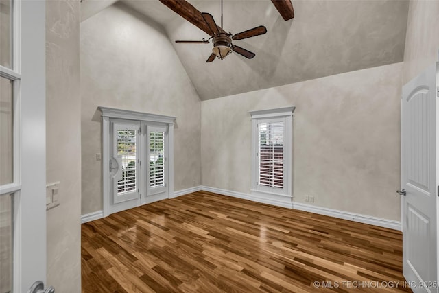 empty room with high vaulted ceiling, a ceiling fan, plenty of natural light, wood finished floors, and baseboards