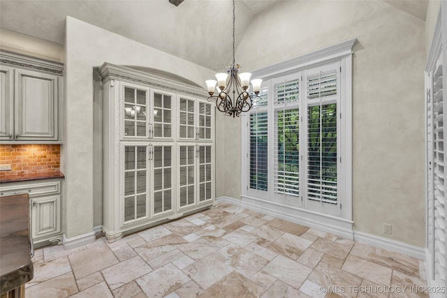 unfurnished dining area featuring stone tile flooring, a chandelier, baseboards, and lofted ceiling