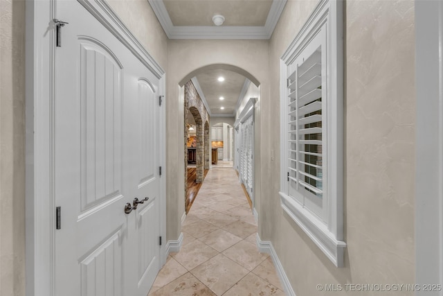 corridor featuring arched walkways, crown molding, baseboards, and light tile patterned floors