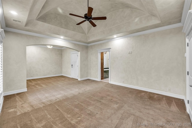 carpeted spare room featuring ceiling fan, arched walkways, crown molding, a tray ceiling, and baseboards