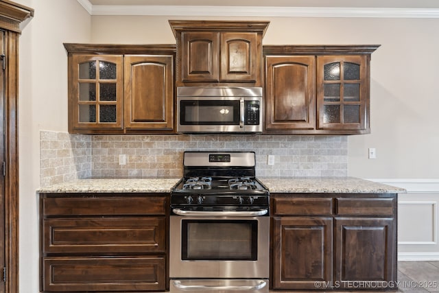 kitchen with appliances with stainless steel finishes, dark brown cabinetry, glass insert cabinets, light stone counters, and ornamental molding