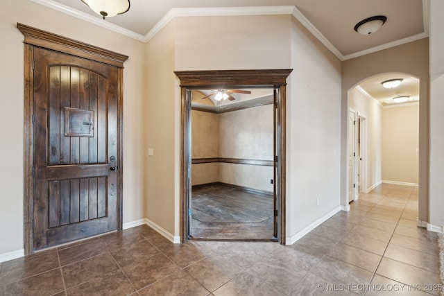 entryway featuring arched walkways, a ceiling fan, ornamental molding, tile patterned flooring, and baseboards