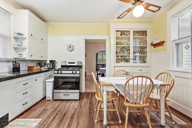 kitchen featuring gas range, open shelves, ceiling fan, crown molding, and light wood finished floors