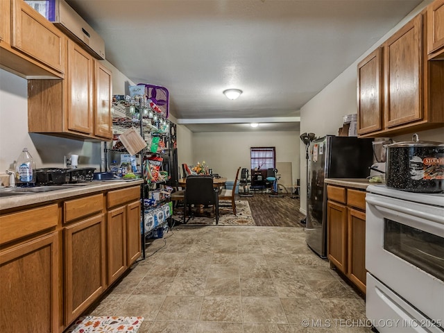 940 N Ross Ave, Dewey, OK 74029 - kitchen featuring stove, freestanding refrigerator, brown cabinetry, and light countertops