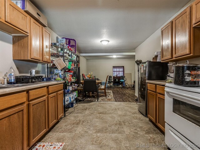 940 N Ross Ave, Dewey, OK 74029 - kitchen featuring stove, freestanding refrigerator, brown cabinetry, and light countertops