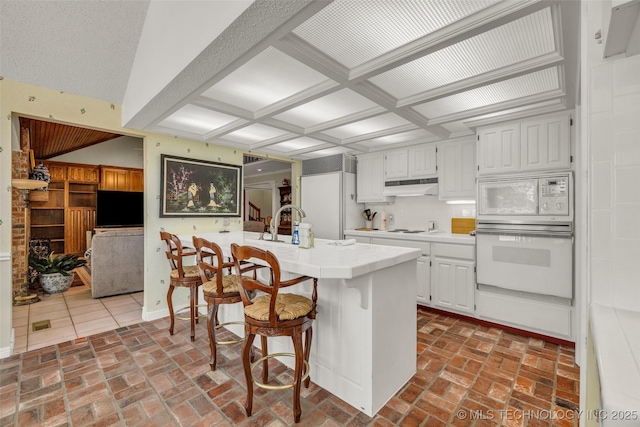 3112 Shore Dr, Grove, OK 74344 - kitchen featuring built in appliances, under cabinet range hood, a breakfast bar area, white cabinets, and brick floors