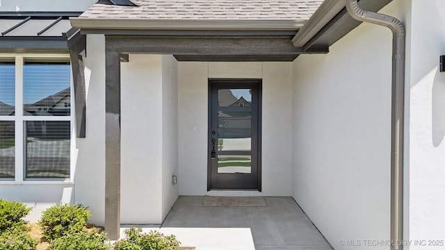 property entrance featuring a shingled roof and stucco siding