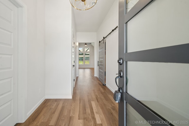 foyer with light wood-style floors, a barn door, baseboards, and a chandelier