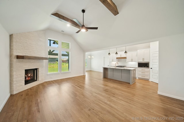 unfurnished living room featuring a sink, ceiling fan, high vaulted ceiling, a stone fireplace, and light wood-style flooring