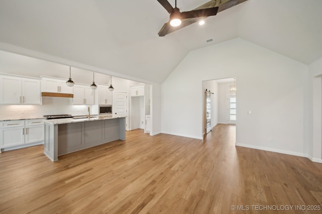 kitchen featuring a ceiling fan, white cabinetry, lofted ceiling, a center island with sink, and decorative backsplash