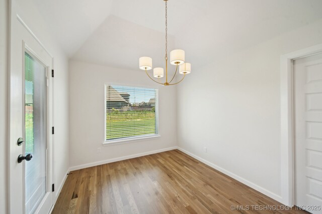 unfurnished dining area with a chandelier, baseboards, wood finished floors, and vaulted ceiling