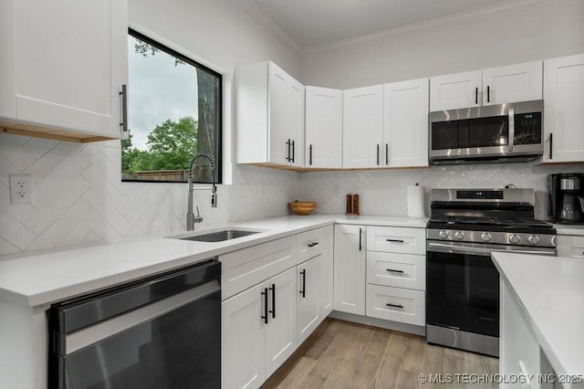 kitchen with stainless steel appliances, a sink, crown molding, light countertops, and white cabinetry