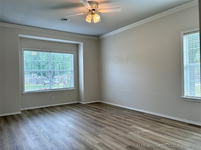 empty room with ornamental molding, wood finished floors, a ceiling fan, and baseboards