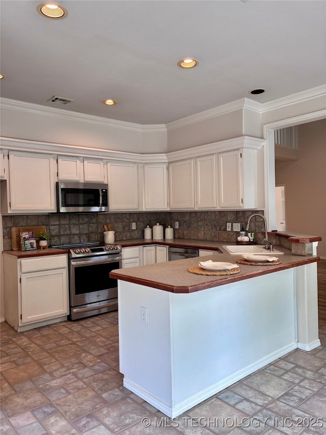 kitchen featuring stainless steel appliances, a sink, a peninsula, crown molding, and white cabinetry