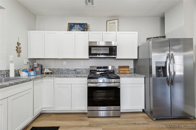 kitchen with appliances with stainless steel finishes, white cabinets, and light stone countertops