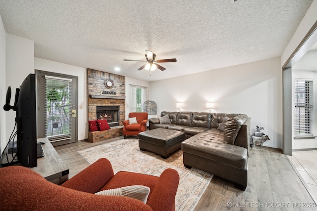 living area with ceiling fan, light wood-type flooring, a fireplace, and a textured ceiling