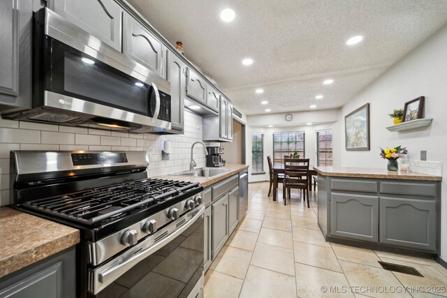 kitchen featuring stainless steel appliances, a sink, a textured ceiling, decorative backsplash, and recessed lighting