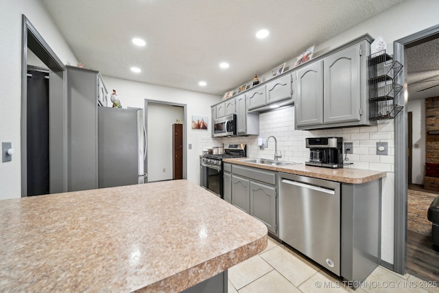 kitchen featuring stainless steel appliances, a sink, gray cabinetry, light countertops, and recessed lighting