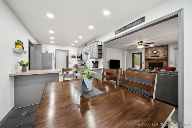 dining space featuring a ceiling fan, wood finished floors, a fireplace, recessed lighting, and a textured ceiling