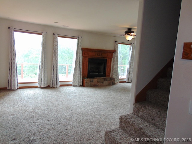 unfurnished living room with carpet, ceiling fan, stairs, and a fireplace with raised hearth