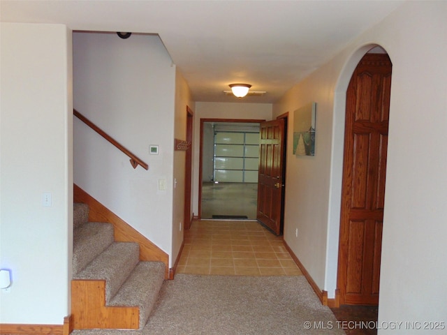hall with stairway, light colored carpet, baseboards, and arched walkways