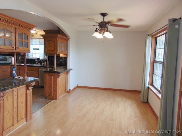 kitchen featuring appliances with stainless steel finishes, brown cabinetry, a ceiling fan, glass insert cabinets, and light wood-style flooring