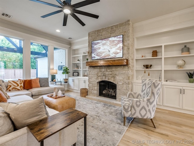 living room with ornamental molding, a ceiling fan, light wood-type flooring, built in shelves, and a fireplace