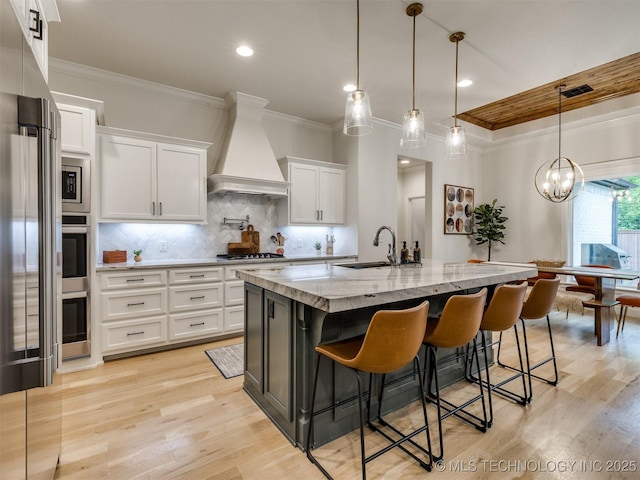 kitchen featuring custom range hood, ornamental molding, a sink, white cabinetry, and light stone counters