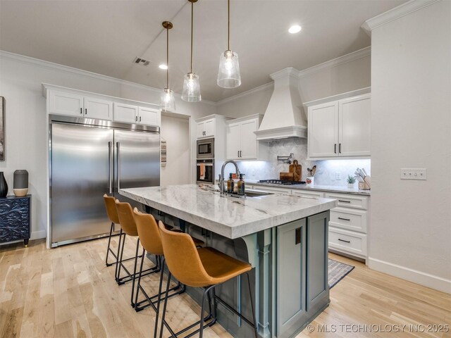 kitchen with built in appliances, premium range hood, tasteful backsplash, white cabinetry, and crown molding